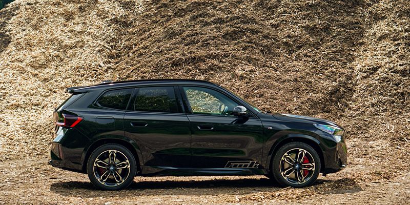 Der vollelektrische BMW iX1 vor einem Haufen Hackschnitzel.